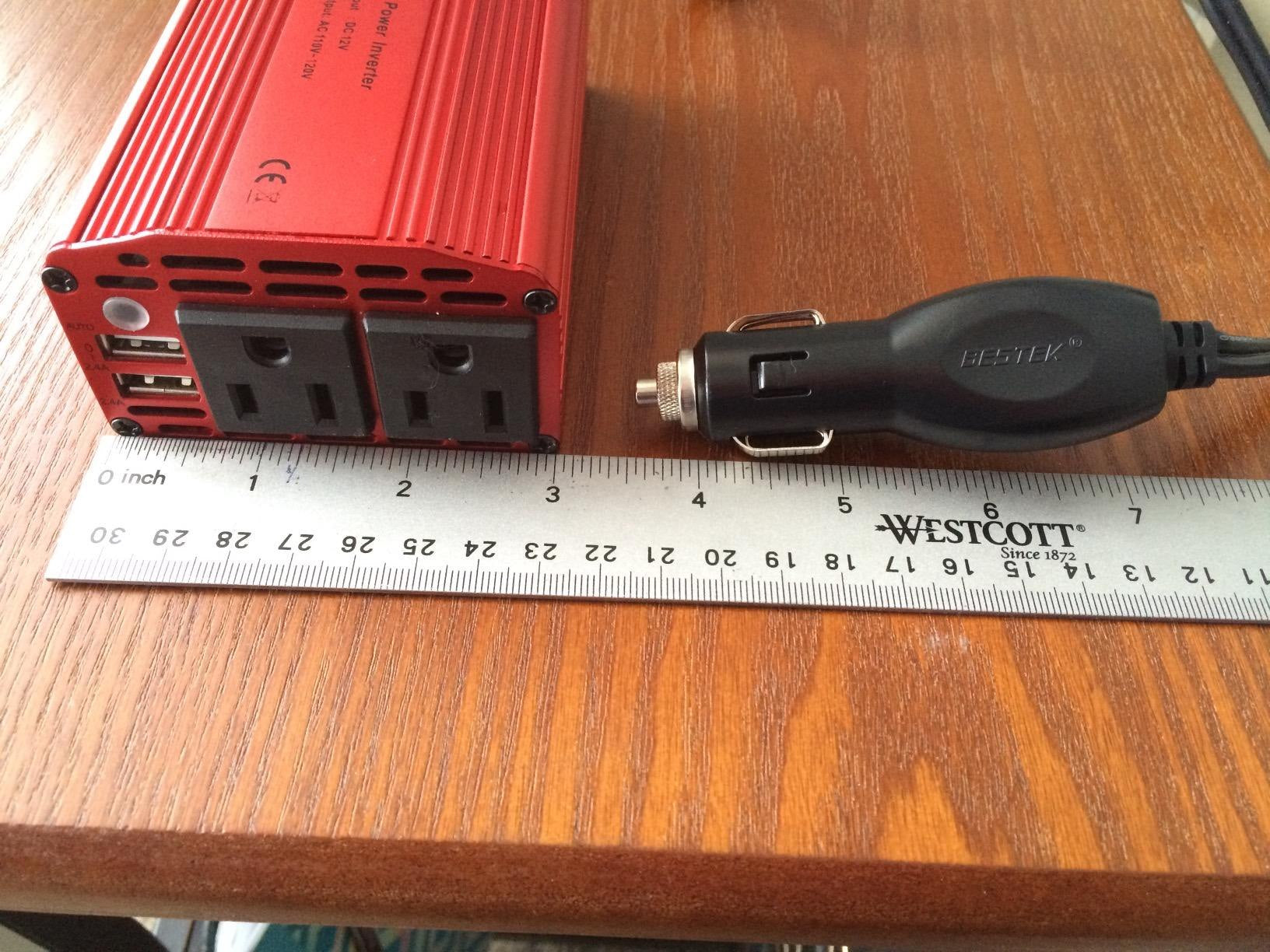 Review photo showing a BESTEK 300W inverter and its car plug beside a ruler.