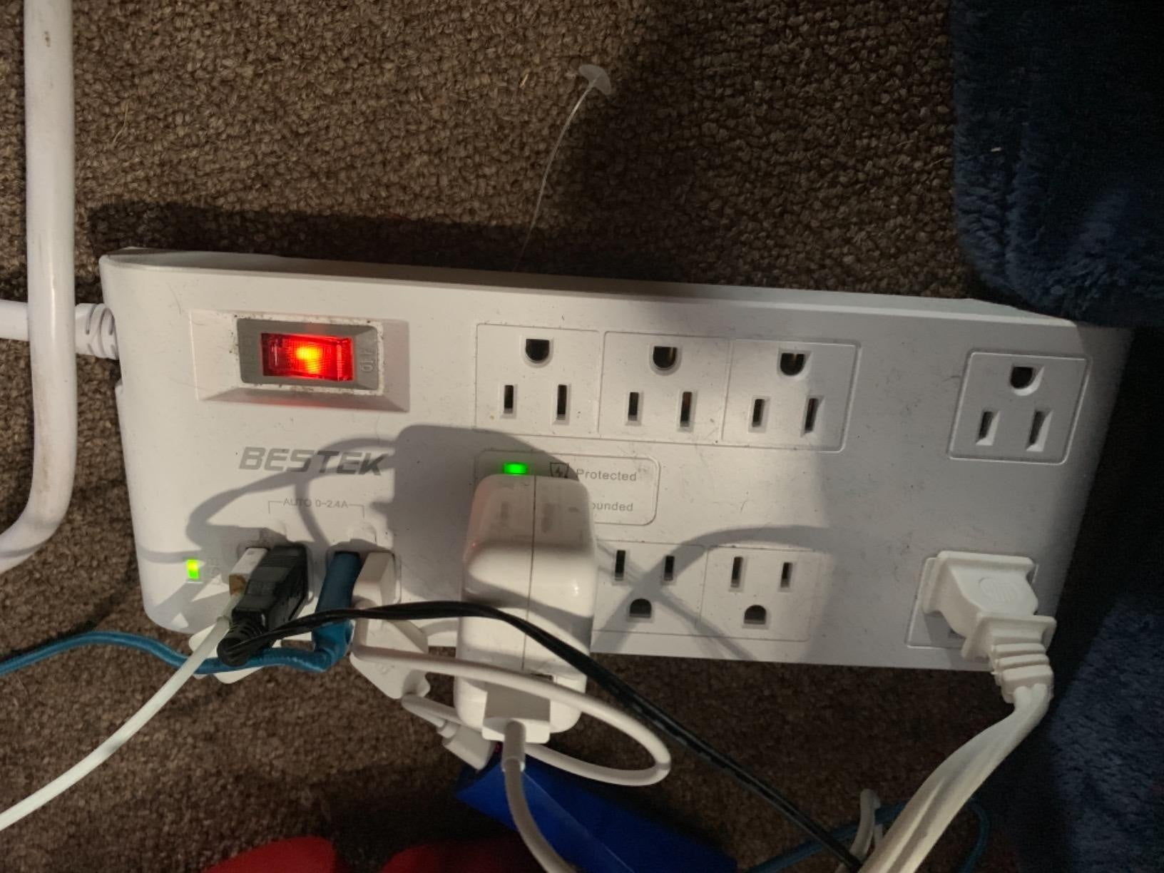 Review photo of a white BESTEK eight-outlet power strip in use.